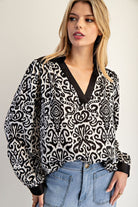Woman wearing a black and white patterned blouse with a plain background
