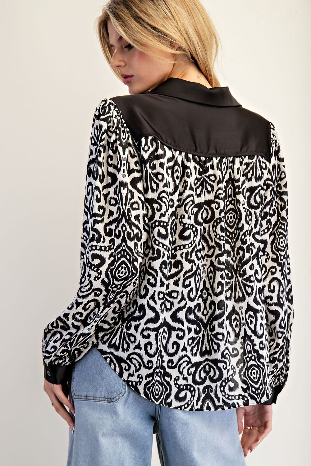 Woman wearing a black and white patterned shirt with a plain black collar on a light gray background