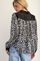 Woman wearing a black and white patterned shirt with a plain black collar on a light gray background