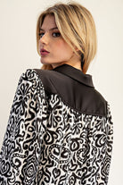 Woman wearing a black and white patterned blouse with a plain background