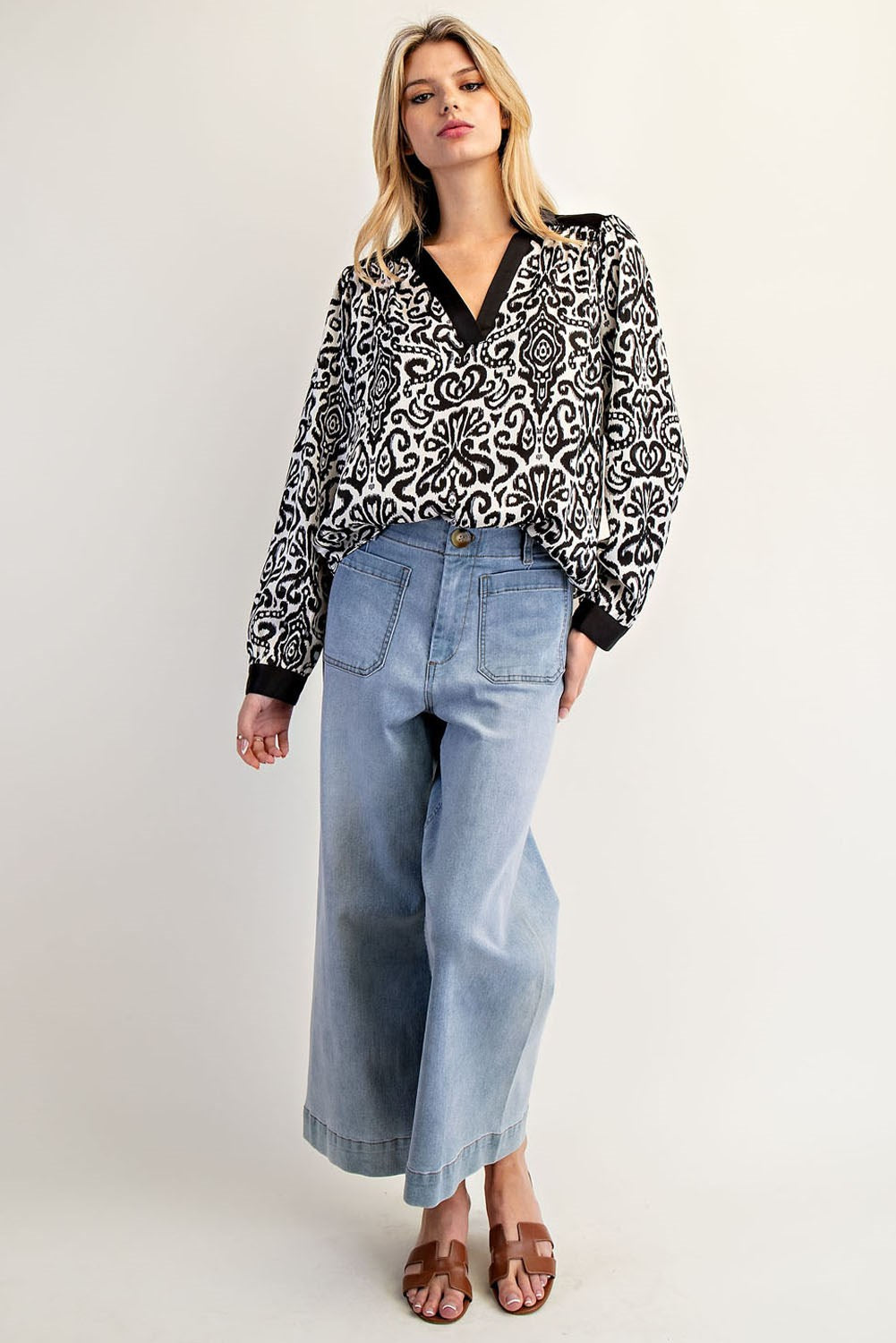 Woman wearing a black and white patterned blouse and light blue jeans on a white background