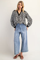 Woman wearing a black and white patterned blouse and light blue jeans on a white background