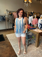 Woman standing in a clothing store wearing a blue and white striped sleeveless top and white shorts.