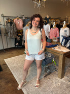 Woman in a light blue dress standing in a store with clothing racks in the background