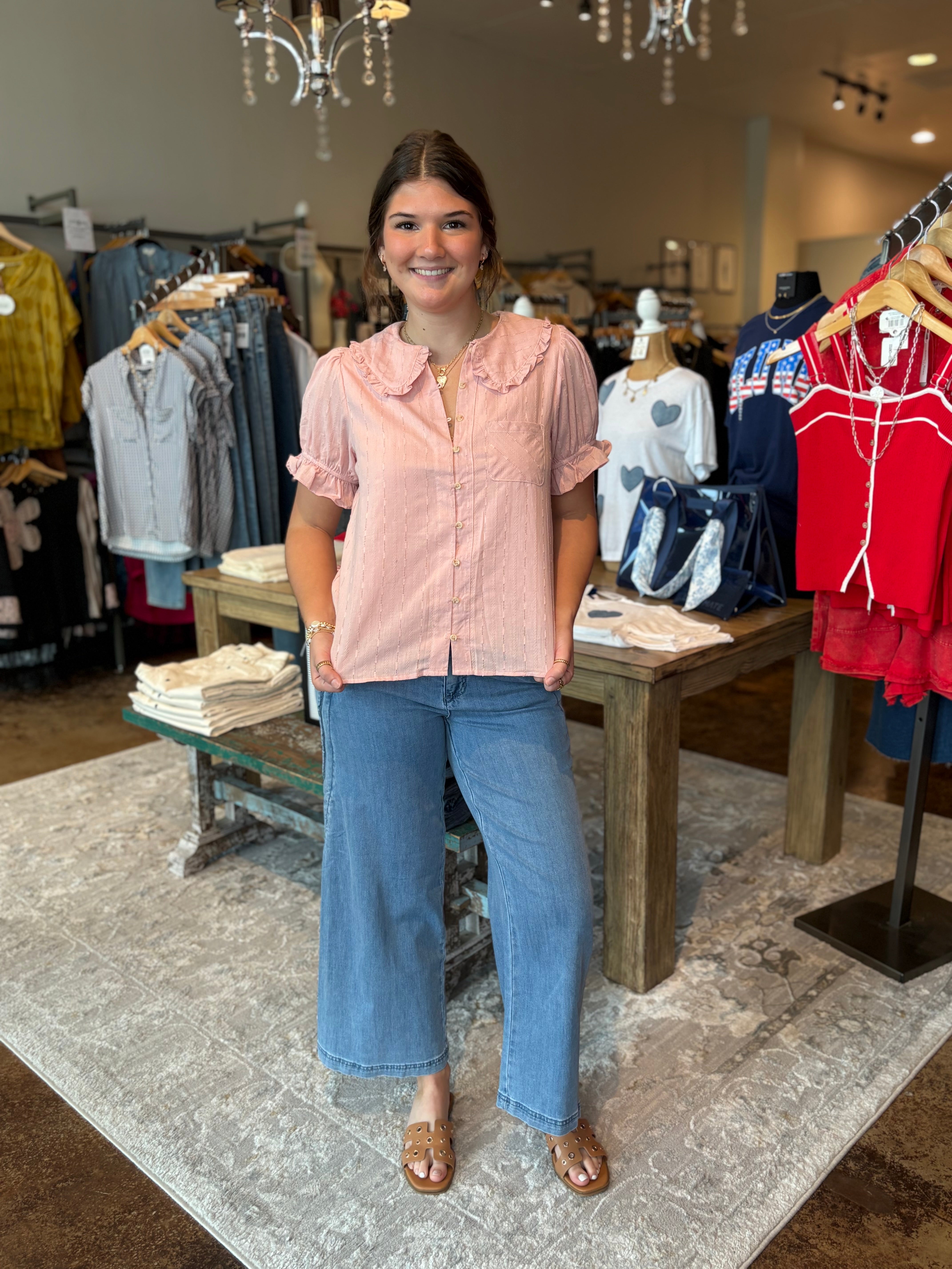 Woman in a pink blouse and blue jeans standing in a clothing store.