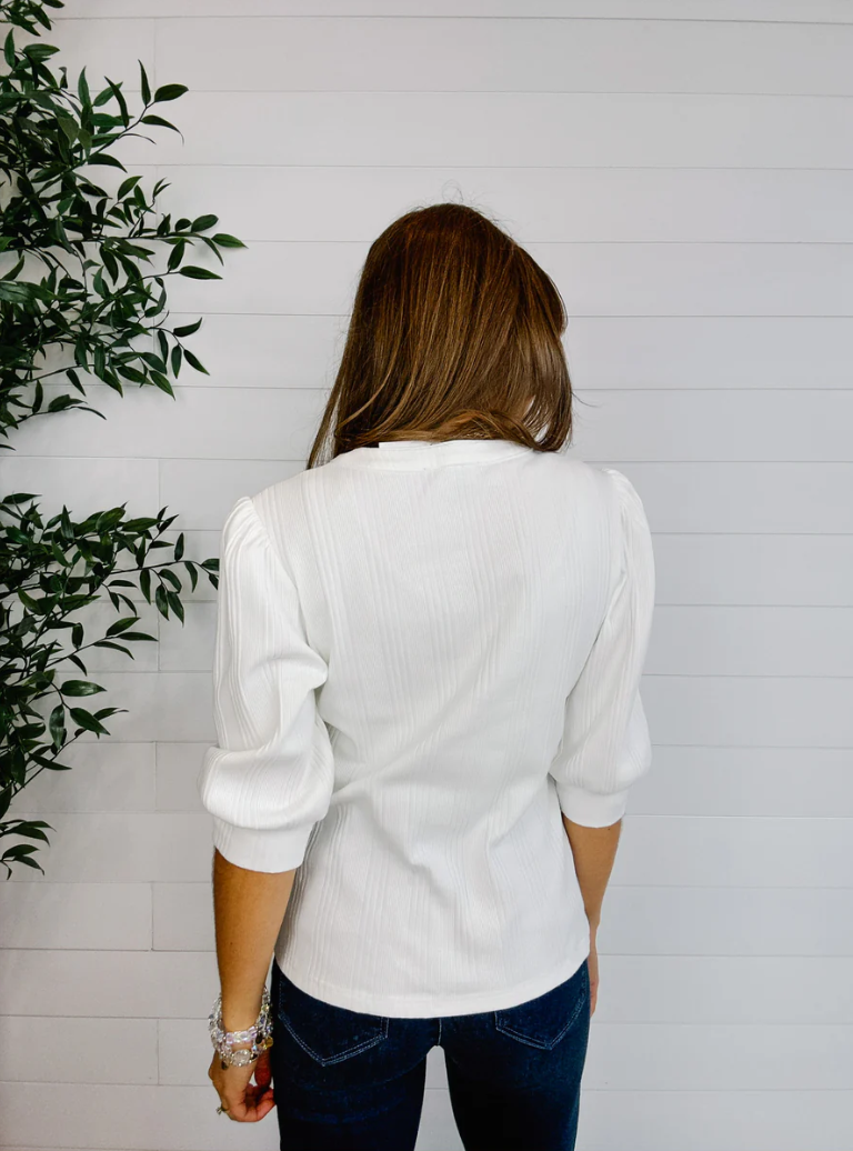 Woman wearing a white blouse with a plant on the left side of the frame
