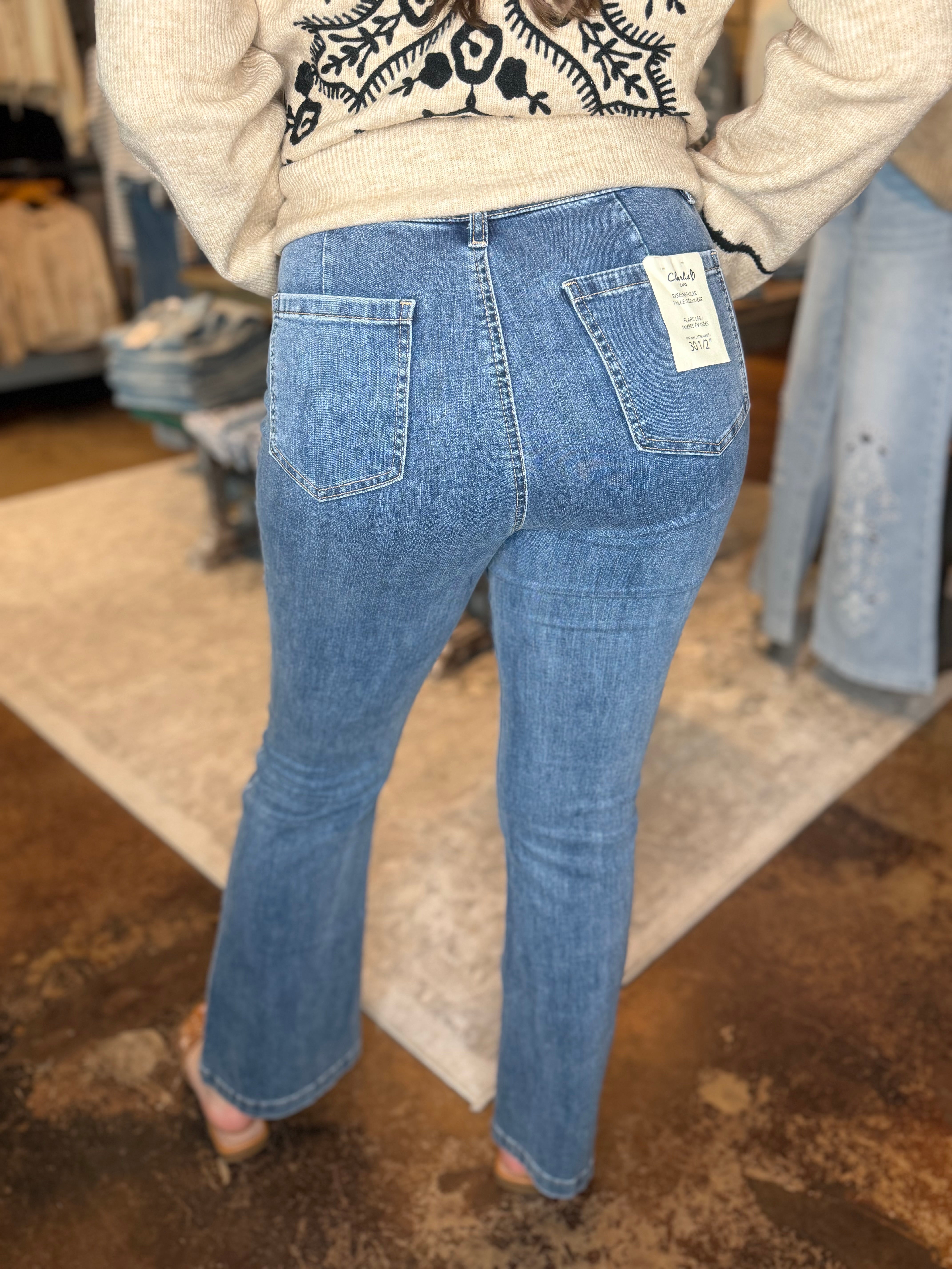 A person shown from the back wearing light blue denim jeans with a visible white size tag on the back pocket, standing in a clothing store.