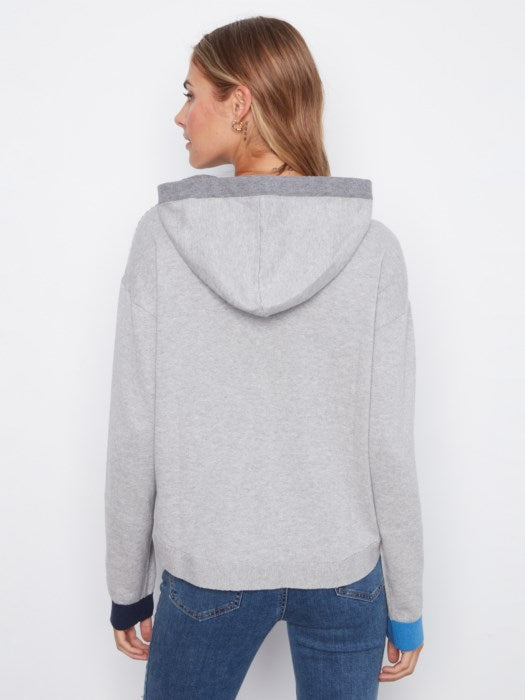 A woman shown from the back wearing a light gray heathered hooded sweatshirt with contrasting dark navy cuffs and hood trim, paired with blue jeans, against a plain white studio background.