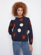 Woman wearing a navy sweater with large polka dots on a plain background