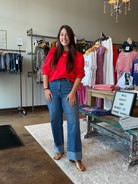 Woman in a red shirt and blue jeans standing in a clothing store.