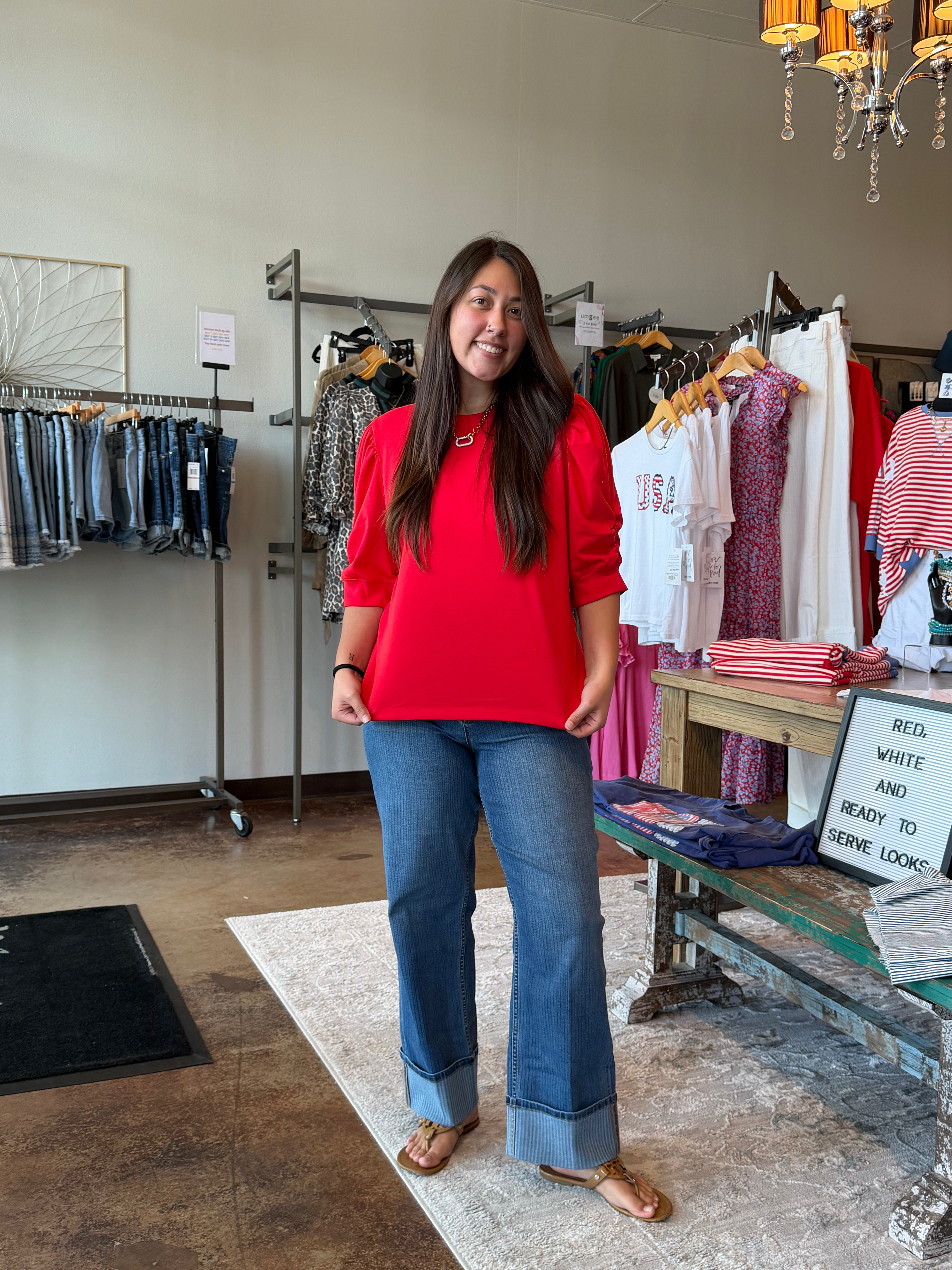 Woman in a red shirt and blue jeans standing in a clothing store.