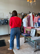 Person wearing a red shirt and blue jeans standing in a clothing store.