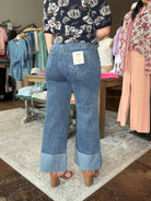 A person shown from the back wearing light-to-medium blue wide-leg denim jeans with rolled cuffs, standing in a clothing store. The jeans have a visible back pocket patch and a white size tag.