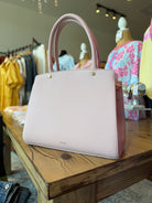 Pink handbag on a wooden table with mannequins and clothing in the background