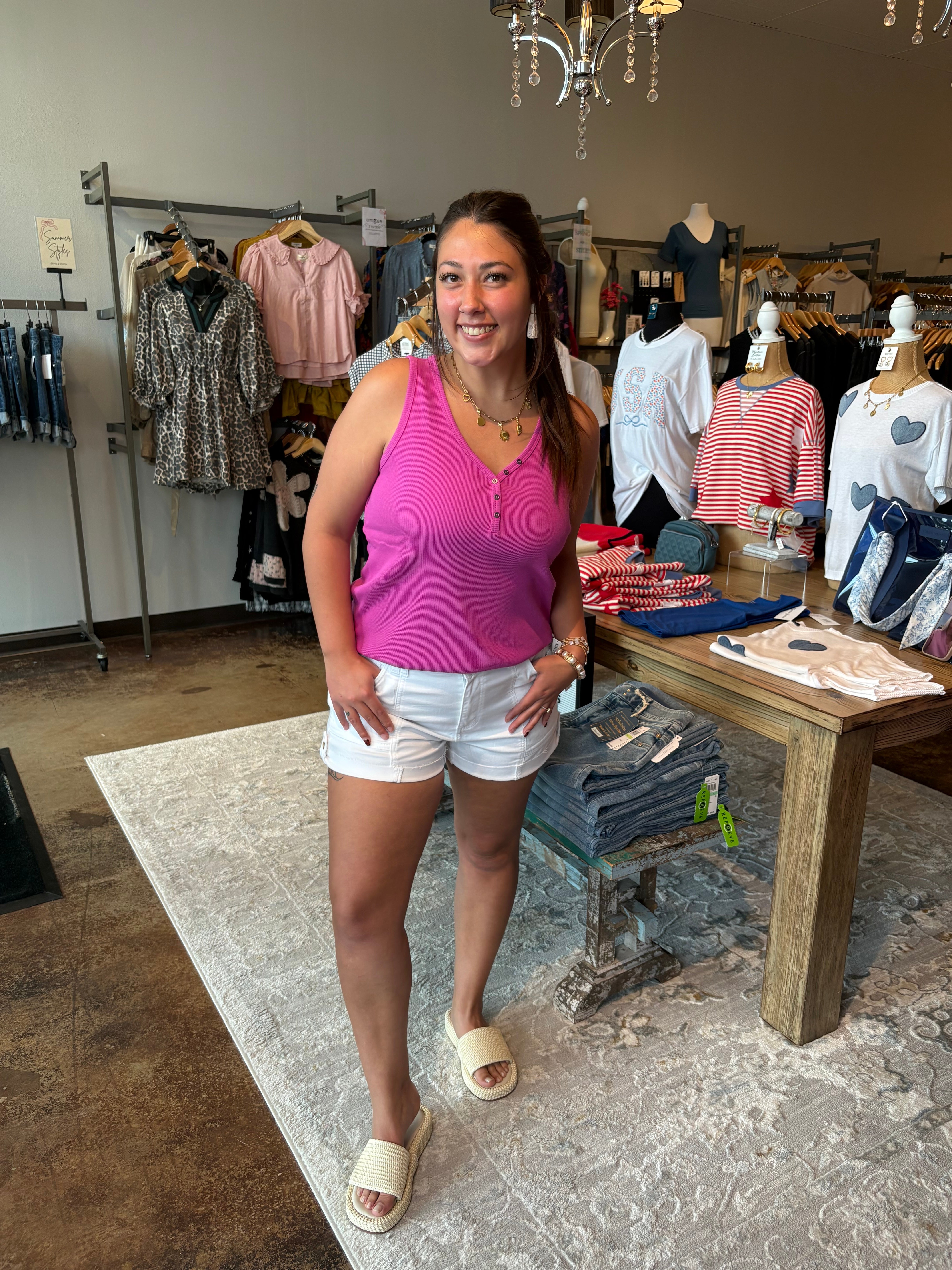 Woman in a pink tank top and white shorts standing in a clothing store.
