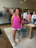 Woman in a pink tank top standing in a clothing store with racks of clothes in the background.
