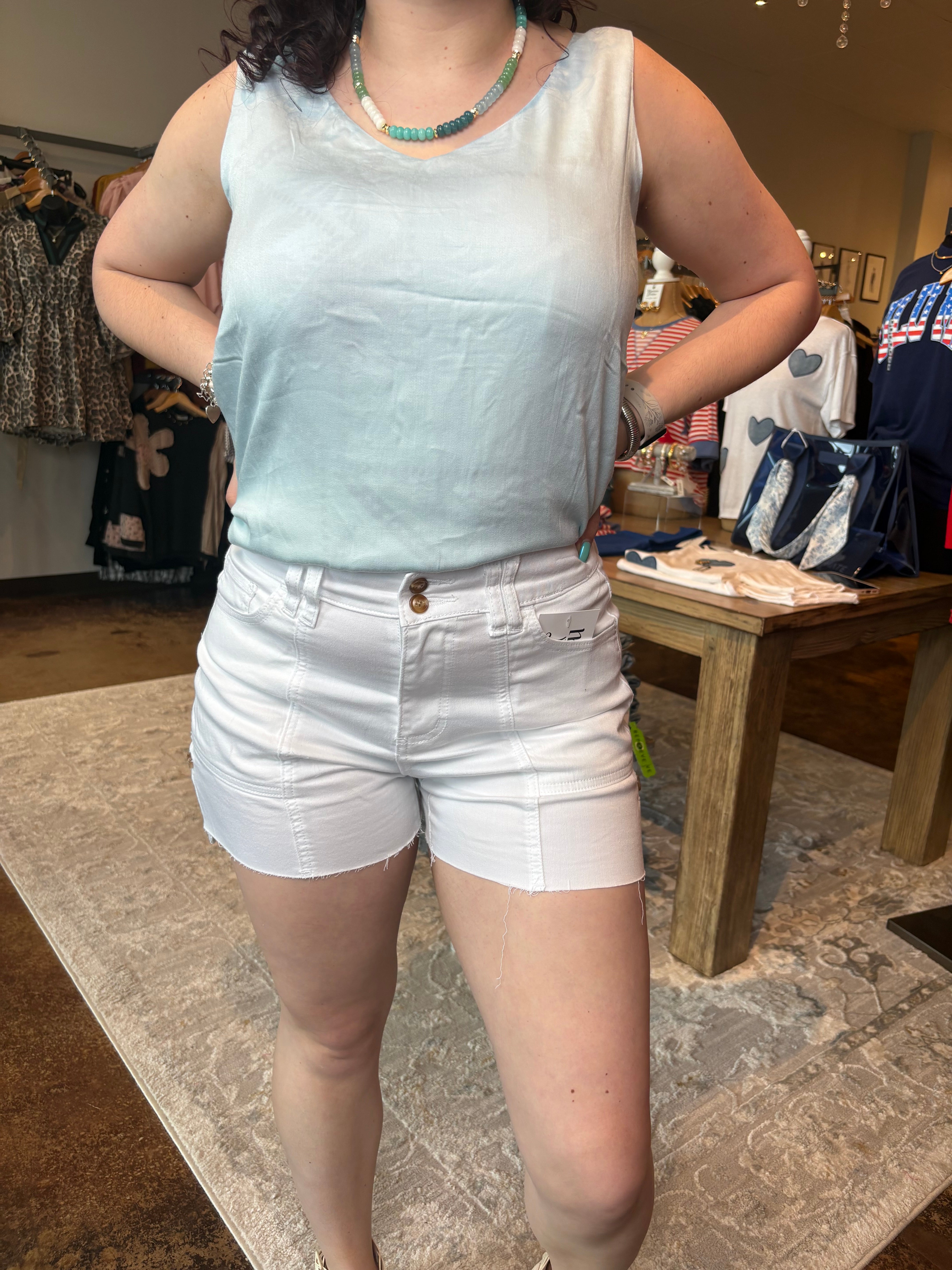 Person wearing a white sleeveless top and shorts in an indoor setting with furniture and boxes.