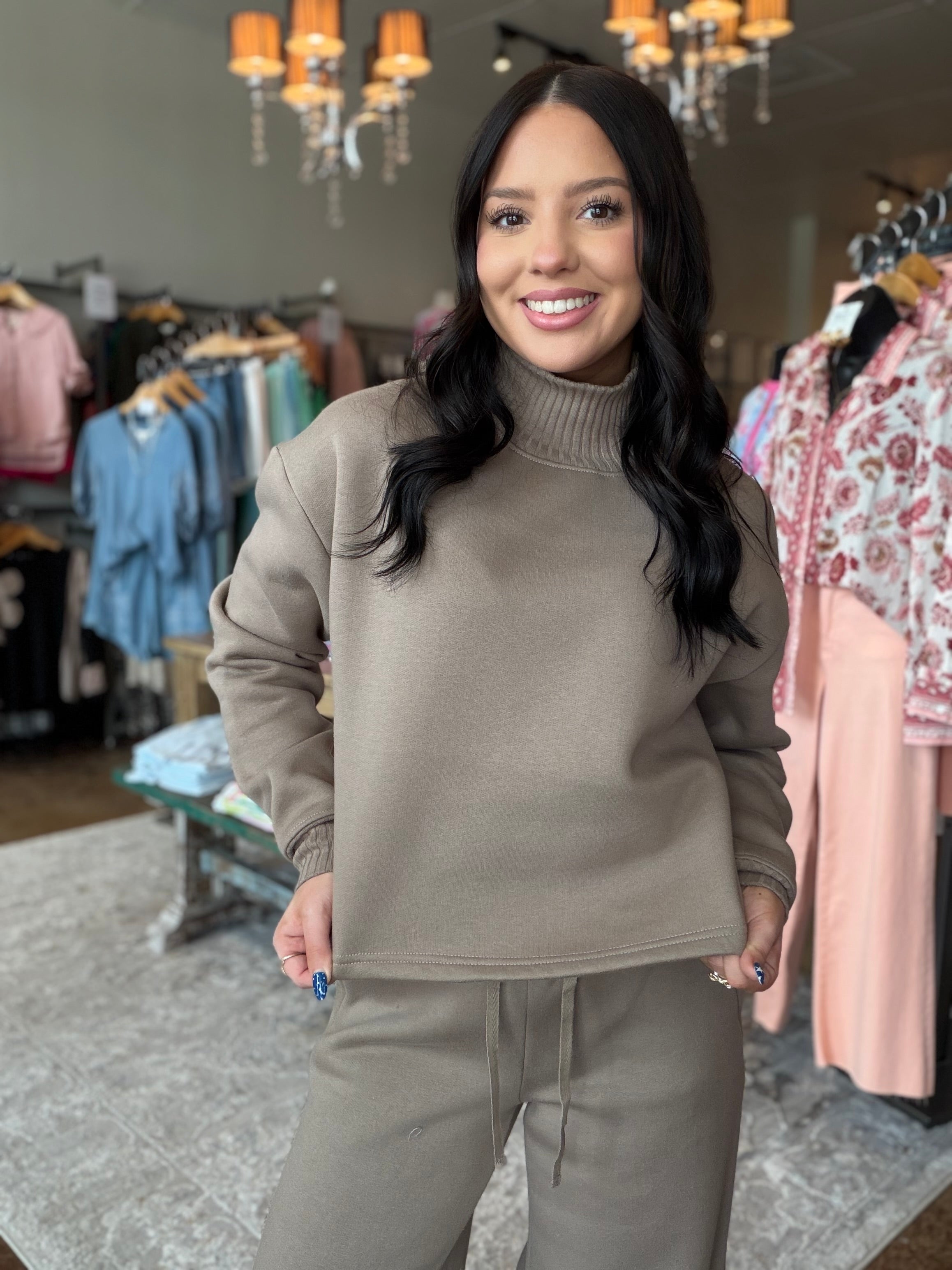 A woman modeling a taupe brown ribbed mock neck sweatshirt and matching sweatpants in a boutique clothing store.