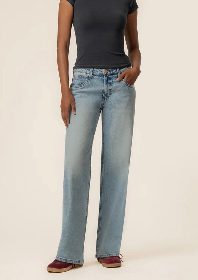 Person wearing light blue jeans and a black top on a beige background