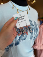 Hand holding a pair of bow-shaped earrings with American flag design on a 'Lansdowne Boutique' card.