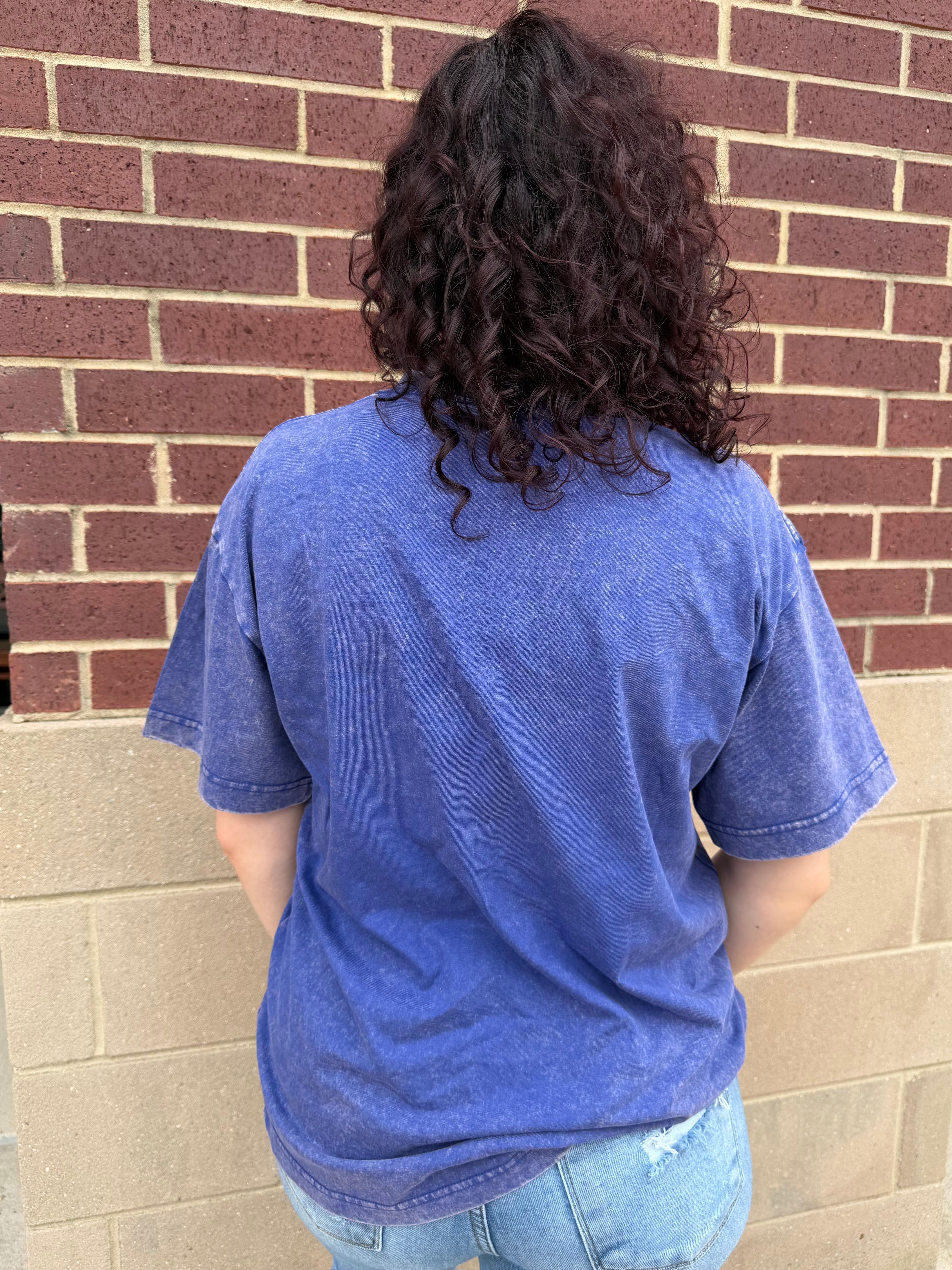 Person wearing a blue t-shirt standing against a brick wall.