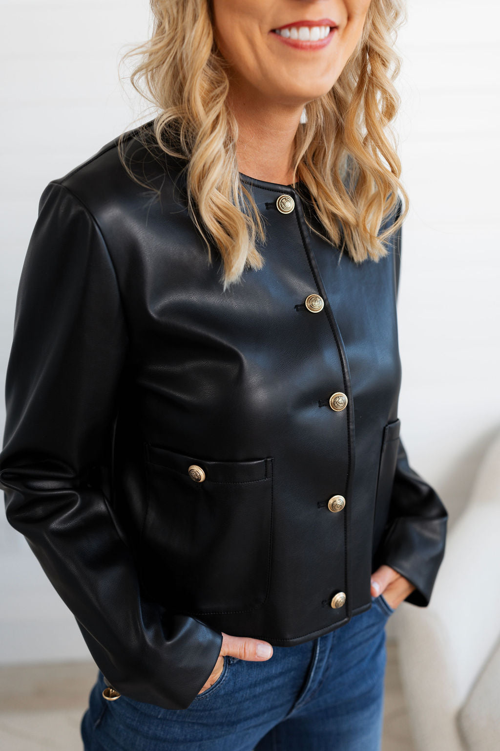 Woman wearing a black leather jacket with gold buttons against a white background