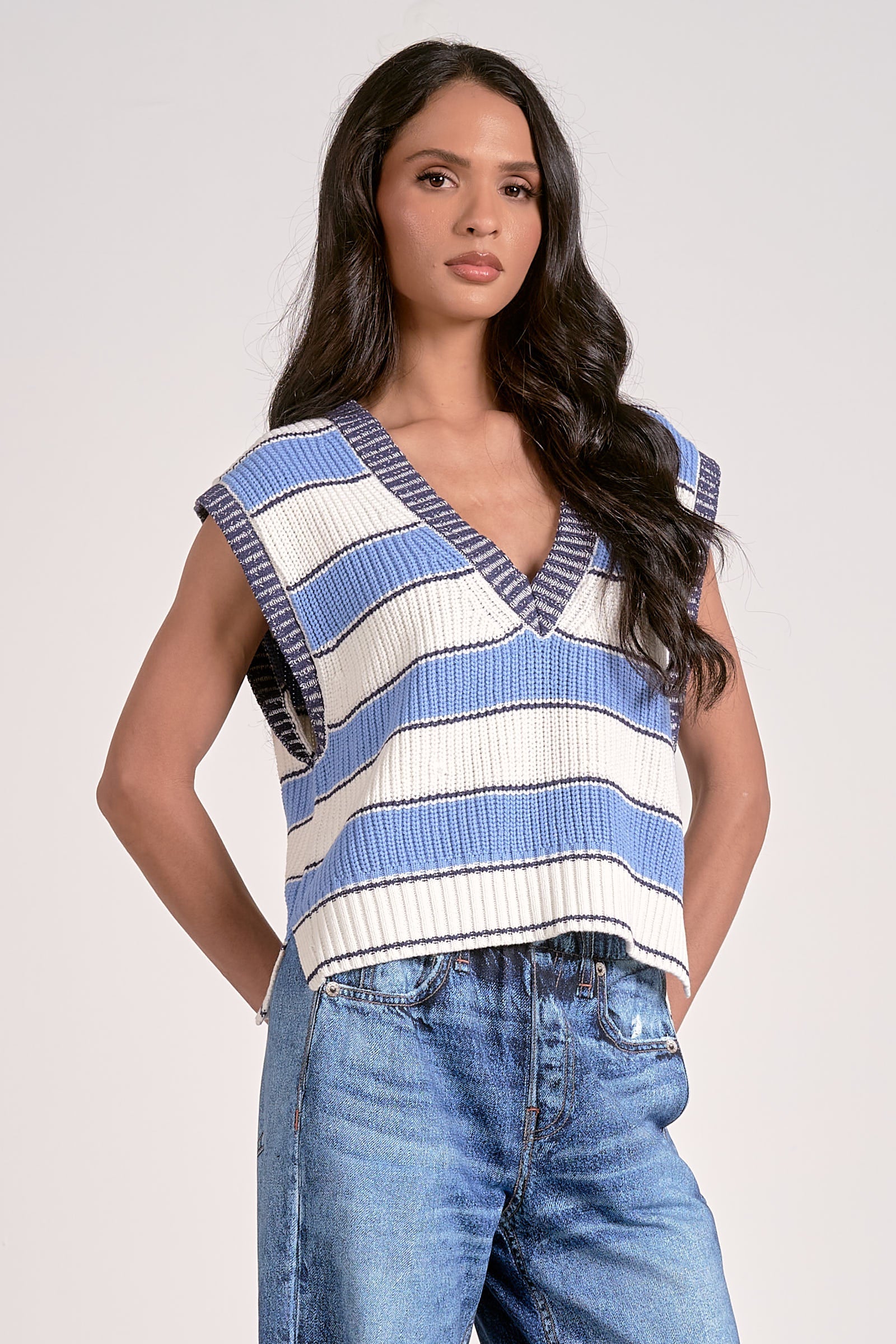 Woman wearing a blue and white striped sleeveless top with jeans on a plain background