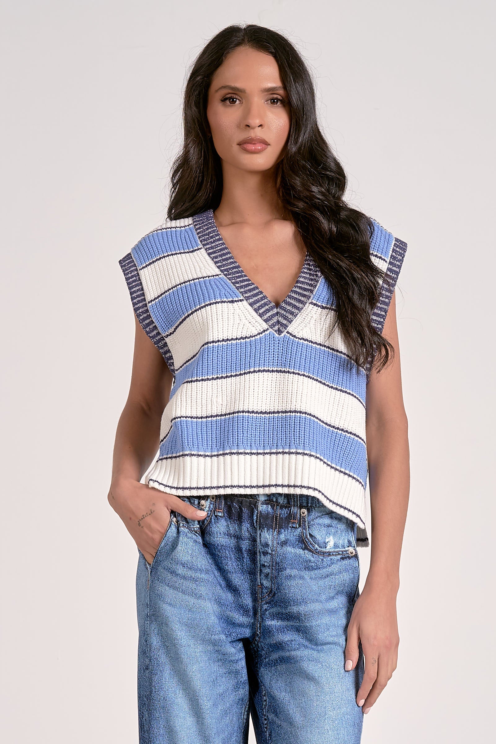 Woman wearing a blue and white striped sleeveless top with jeans on a plain background