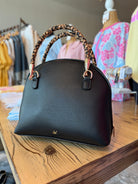 Black handbag with braided handles on a wooden table in a clothing store.