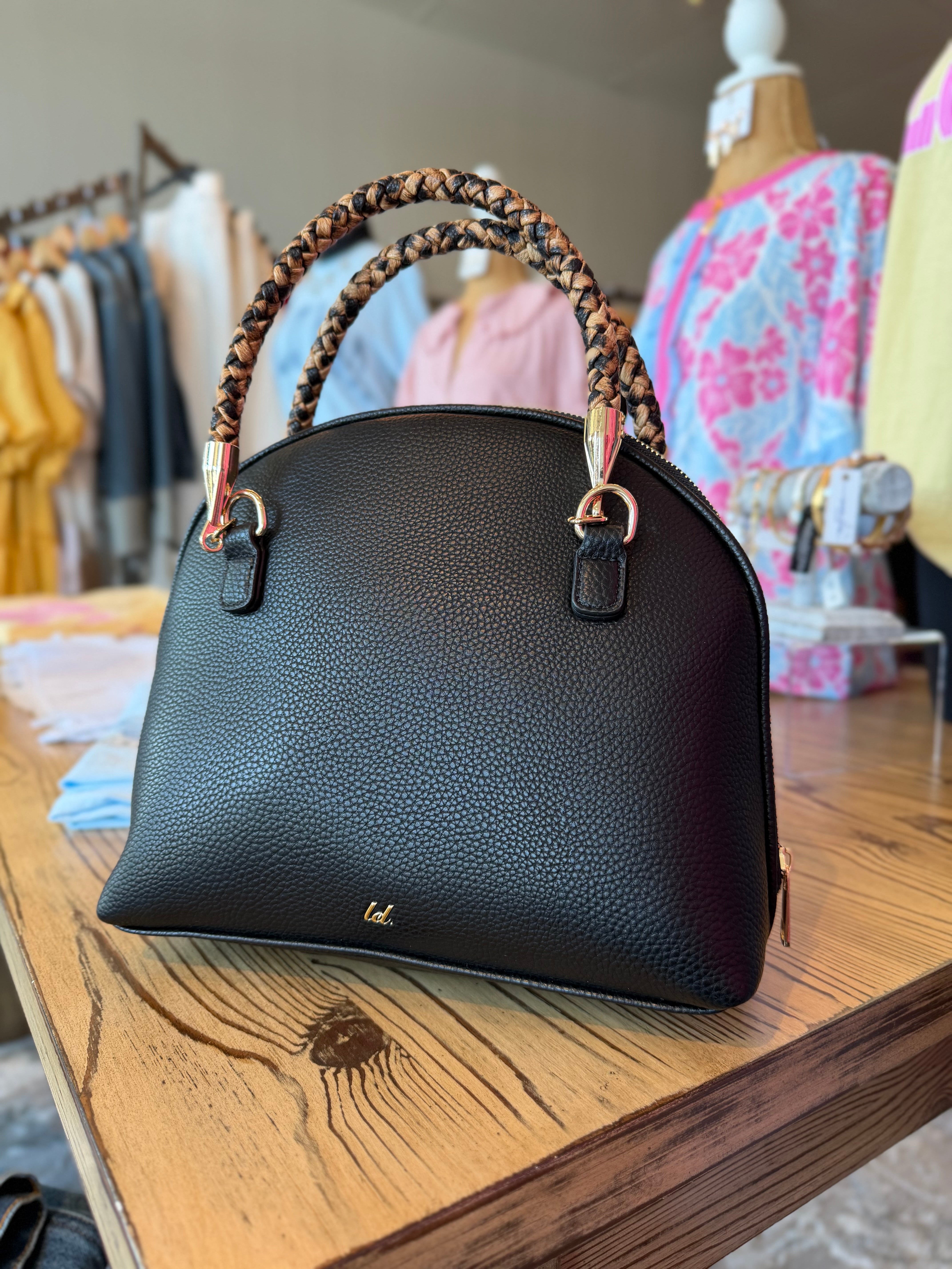 Black handbag with braided handles on a wooden table in a clothing store.