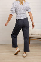 Person wearing a patterned top and dark pants in a room with a wooden floor and white wall.