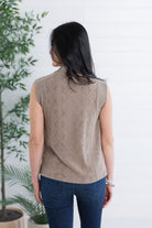 Woman wearing a beige sleeveless knitted top with a white background