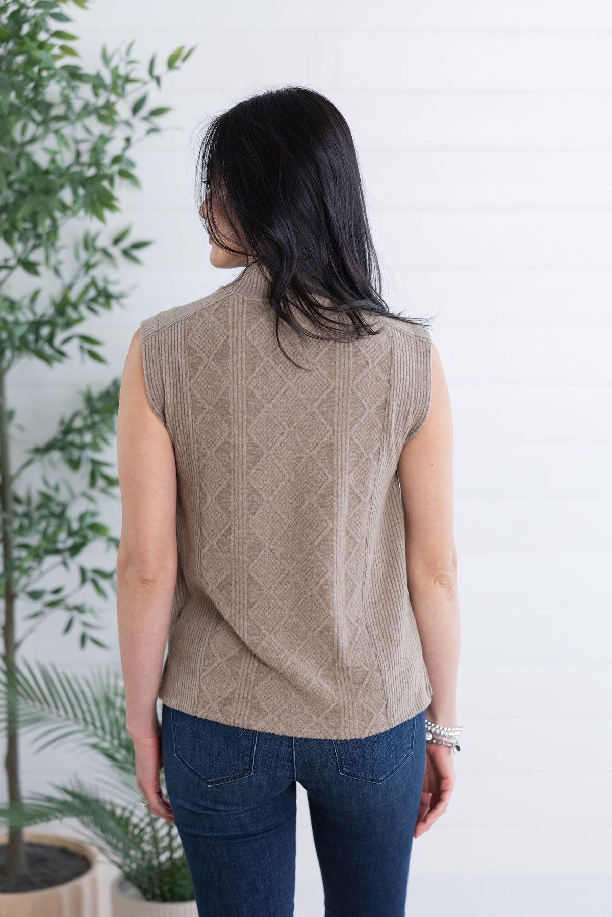 Woman wearing a beige sleeveless knitted top with a white background