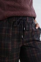 Close-up of a person wearing dark plaid drawstring trousers and a burgundy knit top, with a hand in a pocket.