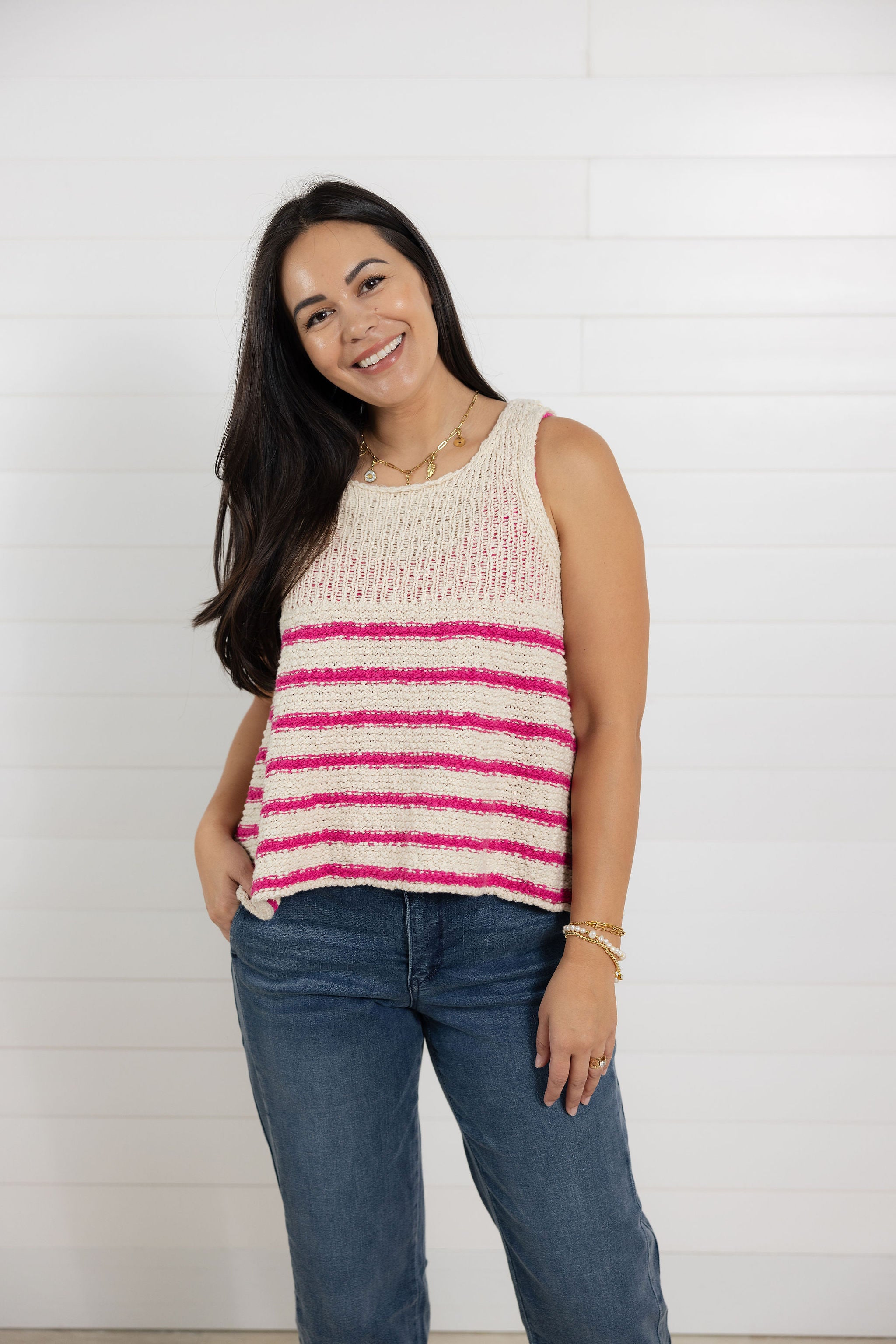 Woman wearing a sleeveless striped top and jeans against a white background