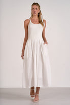 Woman wearing a white sleeveless dress with lace details on a plain background