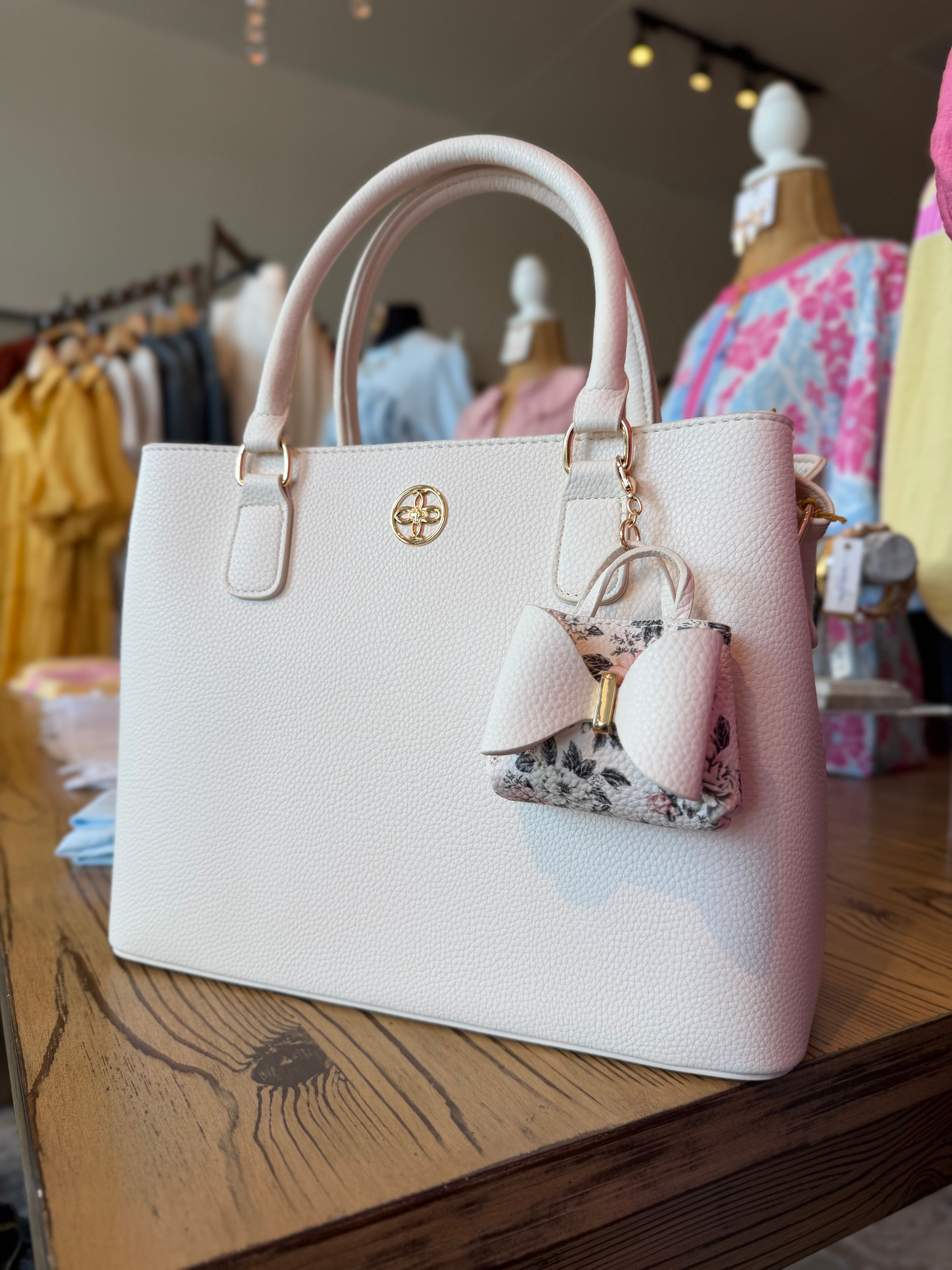 White handbag with decorative keychain on a wooden surface in a store setting