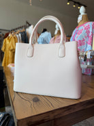 White handbag on a wooden surface with clothing in the background