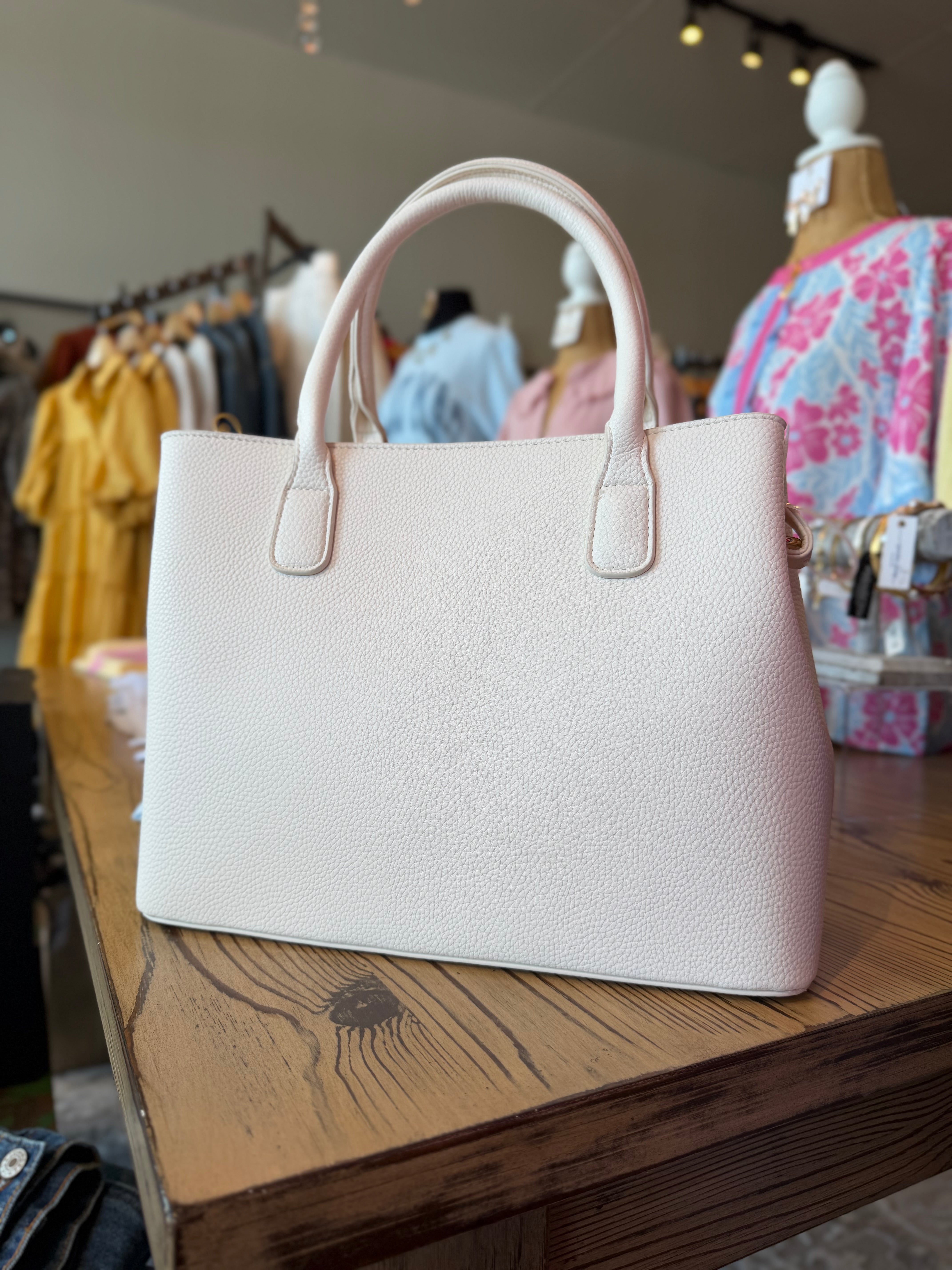 White handbag on a wooden surface with clothing in the background