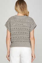 A woman shown from the back wearing a light gray short-sleeve knit top with textured openwork patterns and white pants, against a plain light gray studio background.