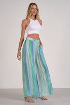 Woman wearing a white top and colorful striped pants on a plain background