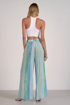 Woman wearing a white top and colorful striped pants on a plain background