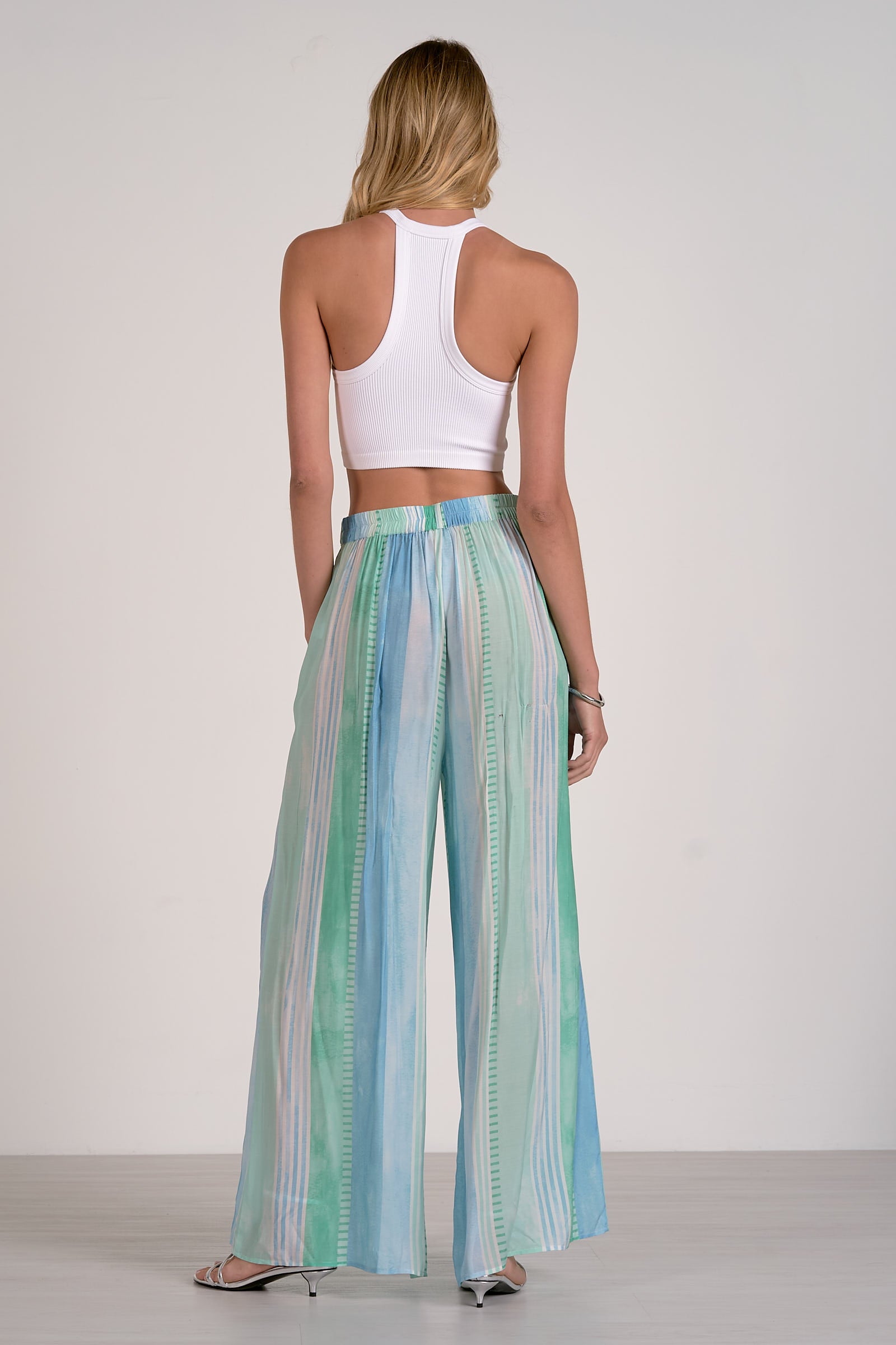 Woman wearing a white top and colorful striped pants on a plain background