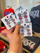 Hand holding packages of earrings with American flag design in a store setting