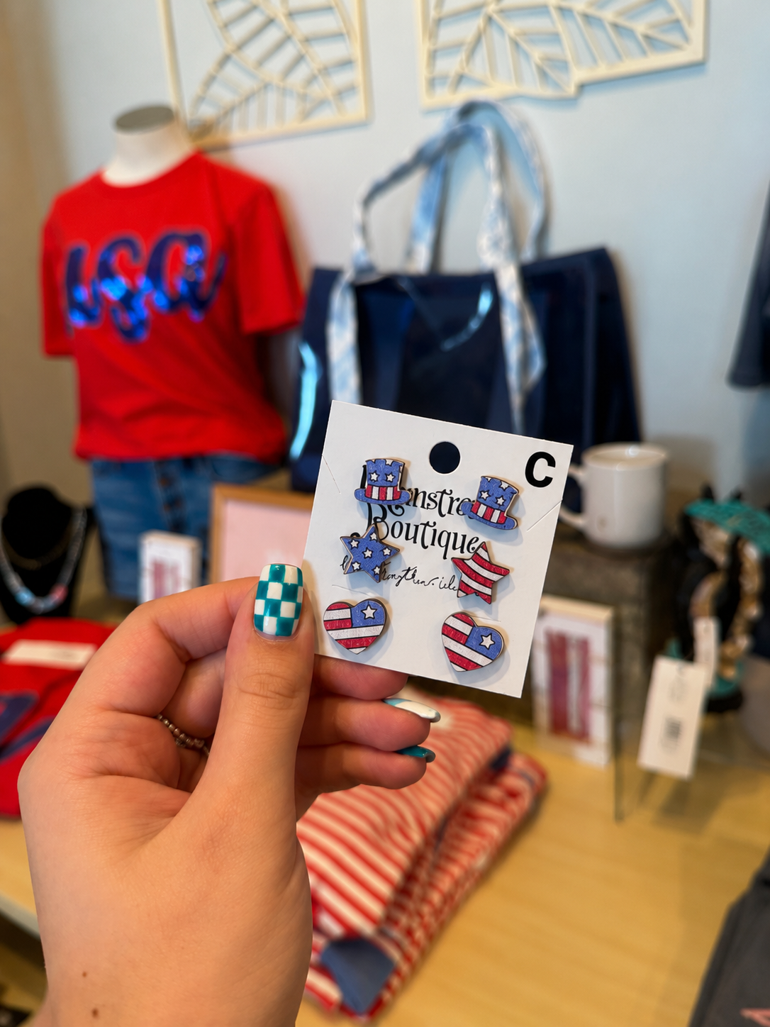 Hand holding a card with American flag-themed earrings in a store setting