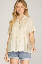 Woman wearing a beige button-up shirt and denim shorts on a plain background