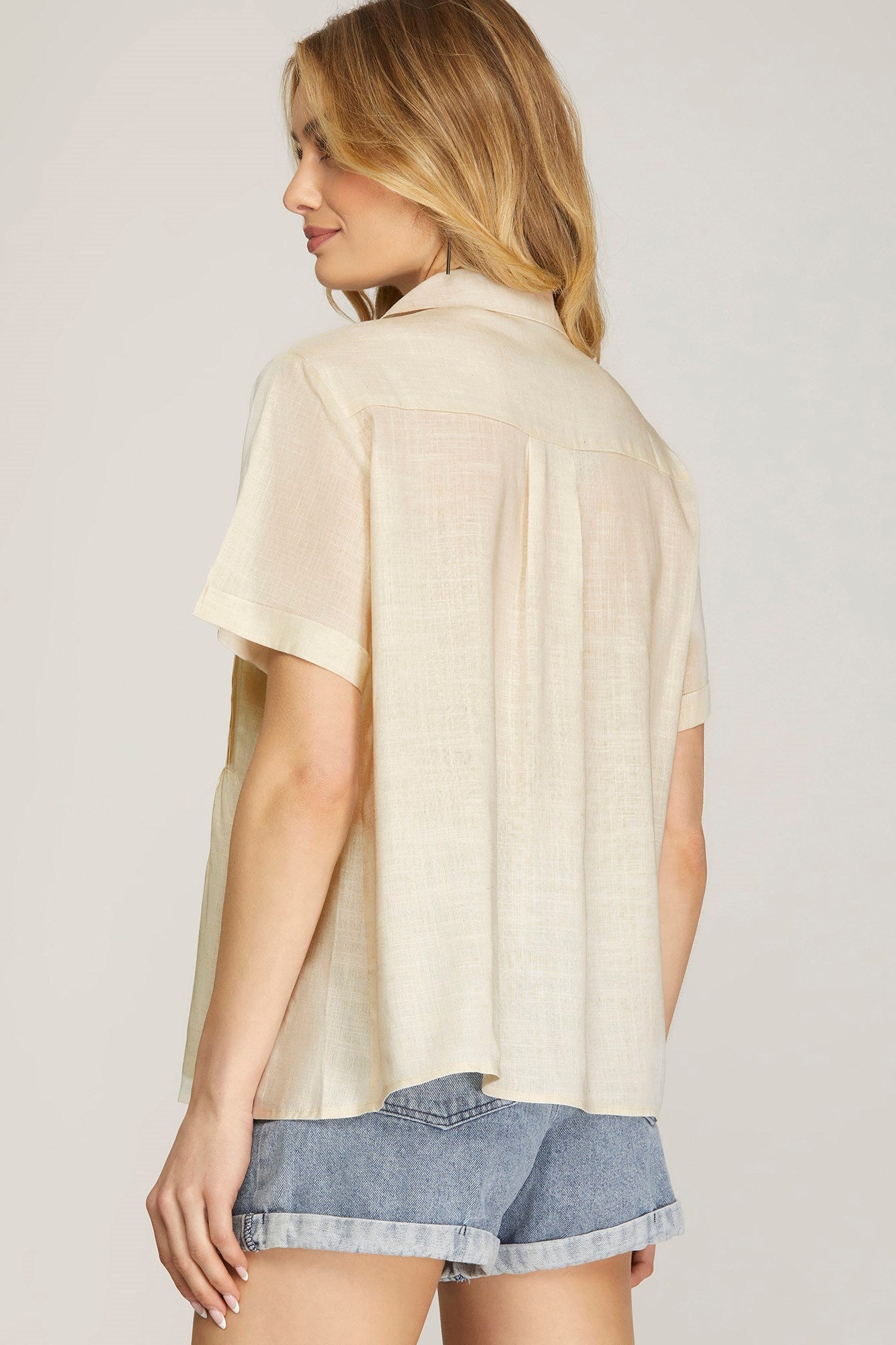 Woman wearing a beige oversized shirt with denim shorts on a plain background