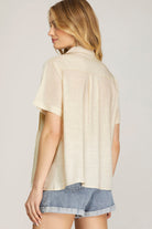 Woman wearing a beige oversized shirt with denim shorts on a plain background