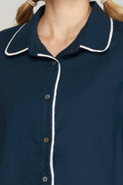 Close-up of a navy blue button-up shirt with white piping trim on the collar and front placket, worn by a model with blonde pigtails.