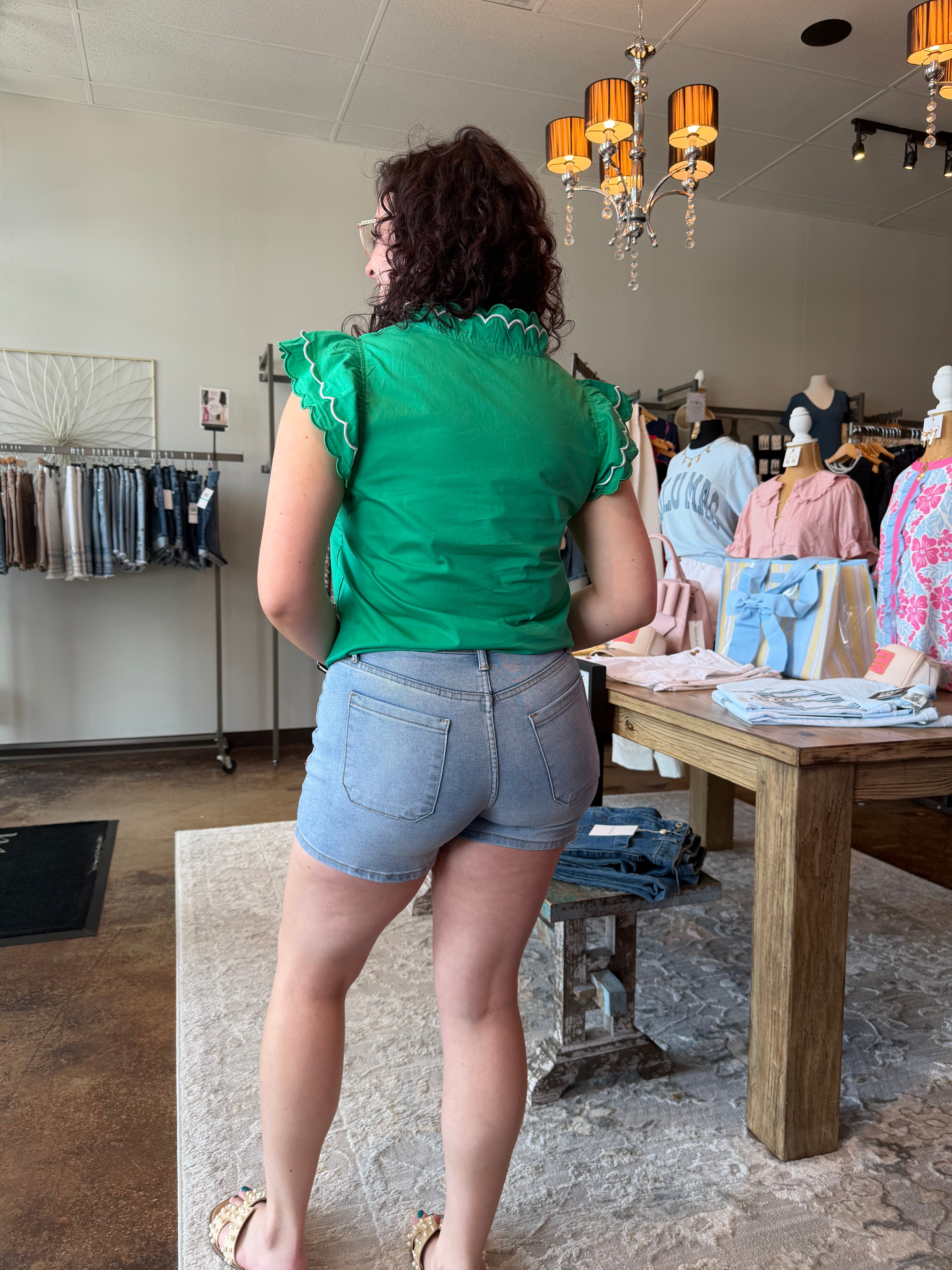 Person wearing a green top and blue shorts standing in a room with furniture and decor.